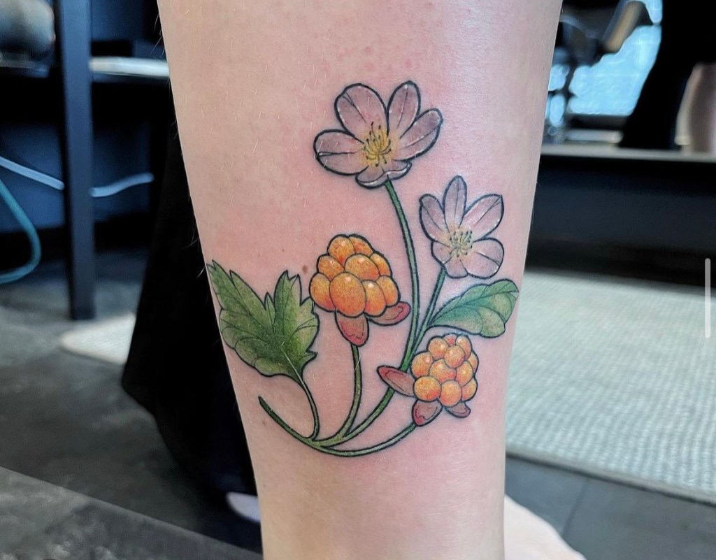 Värikäs tatuointi, jossa on lakkoja, lakankukkia ja vihreitä lehtiä. Tatuointi sijaitsee asiakkaan jalassa.