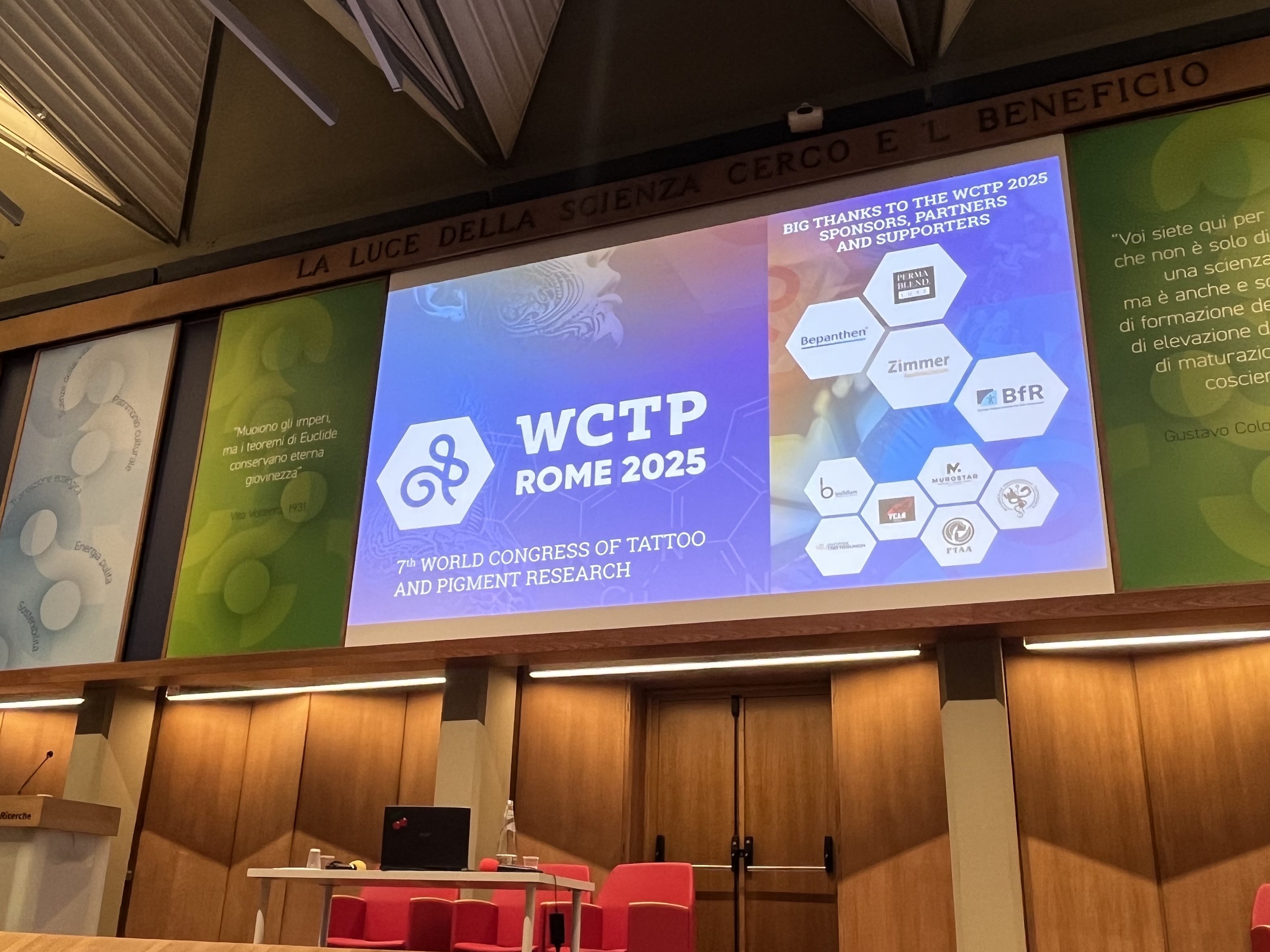 Kuva WCTP 2025 -konferenssin lavalta Roomassa. Näytöllä näkyy tapahtuman logo ja teksti ‘7th World Congress of Tattoo and Pigment Research’, sekä sponsorien logot.